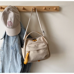 Detail of off-white canvas crossbody bag with yellow zippers on wooden rack