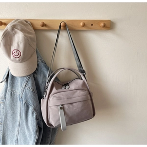 Detail view of light purple canvas crossbody bag with dual handles and grey strap
