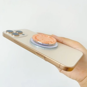 Luxury rose gold coin-shaped magnetic phone grip holder with relief text on a smartphone