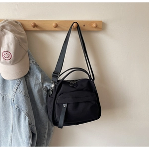 Detail of black nylon tote bag with adjustable strap and front pocket on wood hook