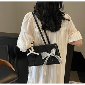 Dettagli dei fiocchi in organza bianca su una borsa a tracolla in pelle nera testurizzata