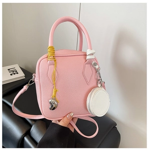 Detail of pink lychee leather handbag featuring a yellow braided cord and heart charm