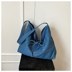 Detail of denim tote bag featuring silver rivet lettering and a bow tie accent