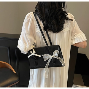 Dettaglio borsa a tracolla nera con fiocco in rete su modella con abito bianco elegante