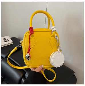 Detail of yellow pebble leather crossbody bag with red woven cord and heart pendant charm