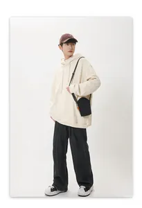 Detail of a beige oversized hoodie with a small black crossbody bag in streetwear style