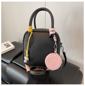 Detail of black lychee grain leather crossbody bag with yellow knot and pink coin purse
