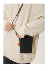 Close-up of black canvas crossbody bag with orange logo tag on a beige hoodie