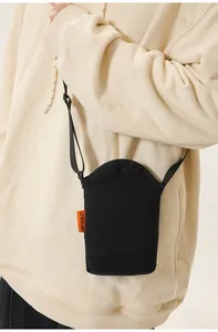 Detail of minimalist black canvas crossbody bag with orange logo tag on white hoodie