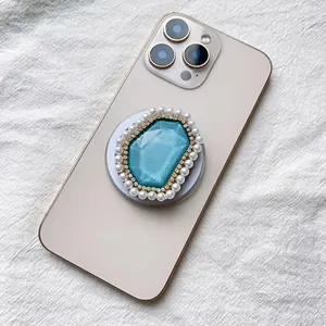 Detail of luxury MagSafe grip with teal crystal, pearls, and rhinestones on gold phone
