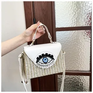 Detail of hand-woven straw bag with evil eye bead embroidery and leather flap