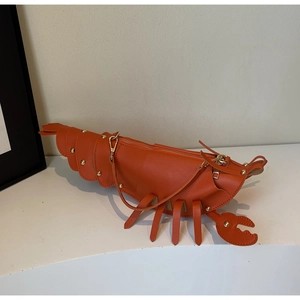 Detail of lobster shaped orange leather crossbody bag with metallic gold rivets
