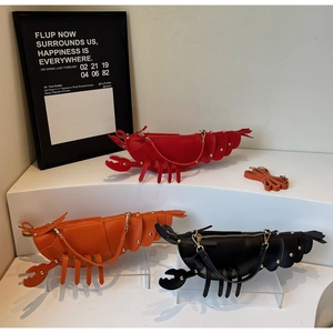 Three lobster-shaped crossbody bags in red, orange and black with gold rivets on display
