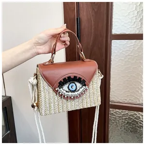Detailed shot of straw woven bag featuring sequined evil eye and brown leather flap