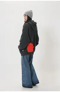 Close-up of red canvas crossbody phone bag on model showing orange side label detail