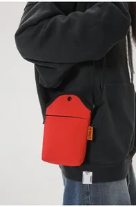 Detail view of red canvas crossbody phone bag featuring a side orange brand label