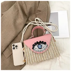 Detail of pink woven crossbody bag with beaded eye design next to a mobile phone