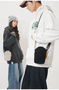 Detail of canvas crossbody bag showing the orange side label and front zipper pocket