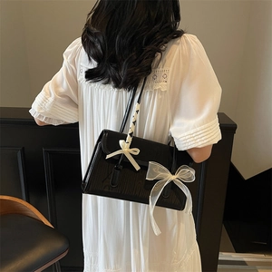 Borsa a tracolla quadrata nera minimalista con fiocco in nastro bianco sulla modella