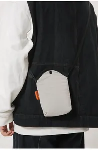 Detail of light grey nylon mini crossbody bag with orange label and black strap