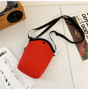 Detail of red canvas crossbody bag with adjustable strap and orange brand tag on a desk