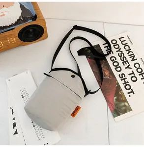 Detail of grey canvas crossbody phone bag with adjustable strap and orange label side