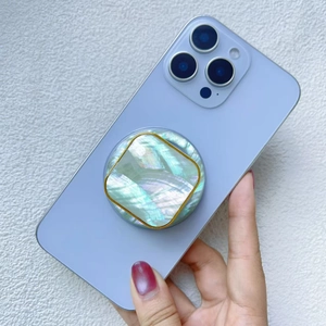 Detail of colorful shell phone grip with gold frame on a blue smartphone held by a hand