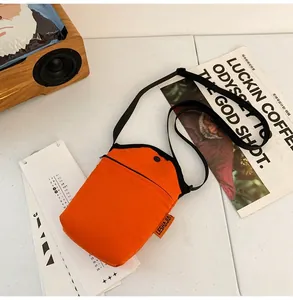 Detail view of the orange fabric crossbody bag with side label and front zipper