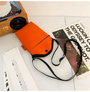 Detail of orange nylon mini bag with adjustable strap and buckle closure on a desk
