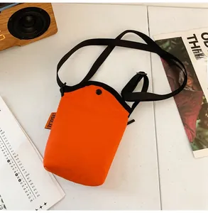 Close-up of orange waterproof nylon crossbody bag with snap button and black strap