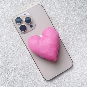 Detail view of a 3D pink heart-shaped padded fabric magnetic phone stand on a gold smartphone