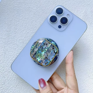 Close-up of circular abalone shell phone stand with gold trim on blue smartphone
