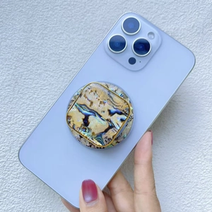 Close-up of a round colorful seashell phone grip with gold metal edge on a purple phone
