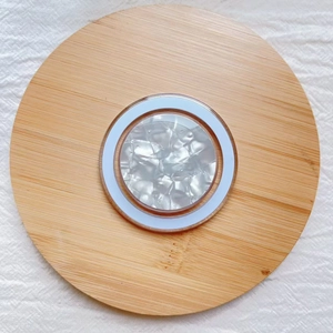 Detail of round MagSafe phone holder with shell pattern on a wooden tray with fabric