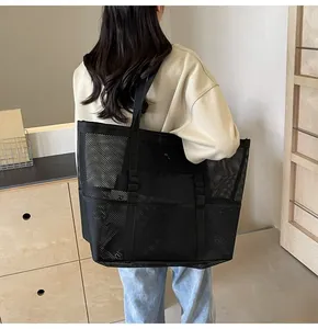 Rear view of a large black mesh tote bag worn on shoulder in a minimalist room