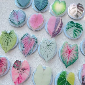 Flat lay of multiple acrylic leaf phone grips showing realistic plant vein patterns