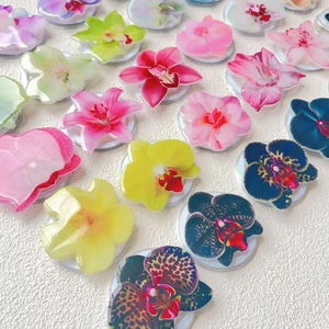 Macro view of diverse acrylic flower phone grips with clear epoxy finish on white fabric