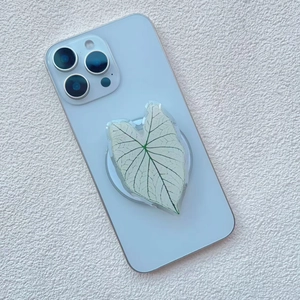 Detail of leaf-shaped acrylic phone grip on blue smartphone with green plant texture