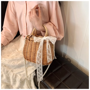 Detail of straw woven bag with white lace bow and elegant pearl shoulder strap