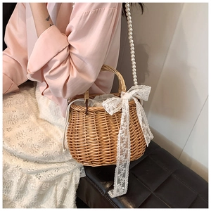 Detail of hand-woven straw basket bag with large white lace bow and pearl strap