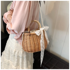 Detail of straw woven bucket bag with lace bow and pearl strap on model shoulder