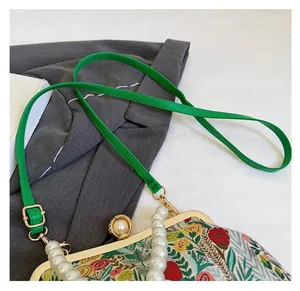 Detail of floral crossbody bag featuring green slim strap and white pearl handle detail
