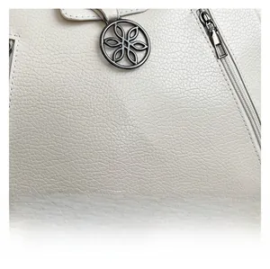 Détail macro du cuir blanc avec un pendentif floral en métal et une fermeture à glissière