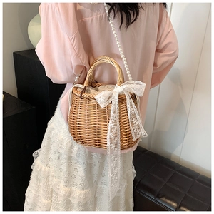 Detail of straw woven bucket bag with white lace bow and faux pearl strap for women