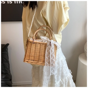 Detail of woven straw bag featuring faux pearl strap and elegant lace ribbon detail