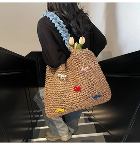Detail of straw tote bag with colorful bows and blue plush strap carried by a model