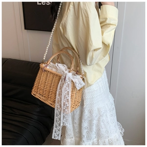 Detail of straw bucket bag featuring large lace bow and pearl strap worn by a model