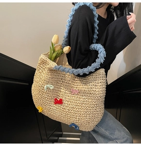 Detail of straw woven tote bag featuring colorful crochet bows and blue fuzzy shoulder strap