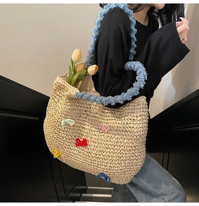 Detail of straw woven tote bag featuring colorful crochet bows and blue fuzzy shoulder strap
