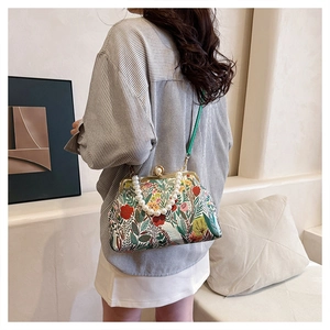Detail of floral printed bag featuring a white pearl handle and green leather strap